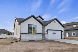 View of front of house with driveway, stone siding, stucco siding, and a garage