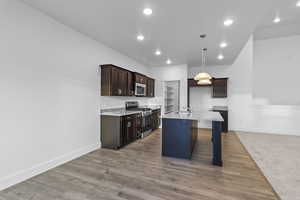 Kitchen with stainless steel appliances, a breakfast bar, light wood-style floors, a center island with sink, and light stone countertops