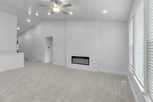 Unfurnished living room with a ceiling fan, a fireplace, lofted ceiling, recessed lighting, and light colored carpet