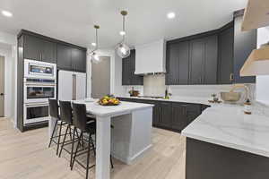 Kitchen featuring light stone countertops, hanging light fixtures, white appliances, a breakfast bar, and light wood-style flooring
