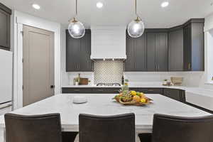 Kitchen with a kitchen bar, light stone counters, hanging light fixtures, backsplash, and a center island