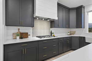 Kitchen featuring light stone counters, decorative backsplash, and stainless steel gas stovetop