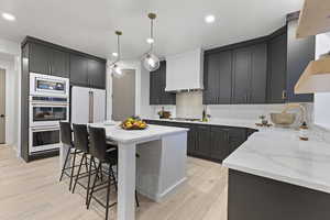 Kitchen with light stone counters, decorative light fixtures, a kitchen breakfast bar, white appliances, and a center island