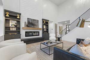 Living room featuring a large fireplace, light wood-type flooring, built in shelves, and a high ceiling