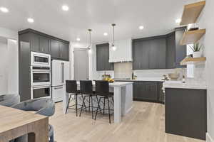 Kitchen featuring open shelves, a breakfast bar, gray cabinetry, decorative light fixtures, and a center island