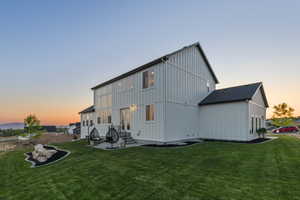 Back of property at dusk featuring board and batten siding, a lawn, and entry steps