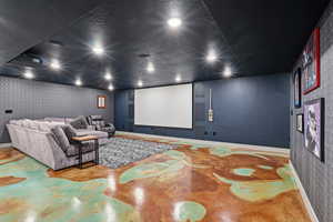 Home theater featuring wallpapered walls, finished concrete flooring, and a textured ceiling