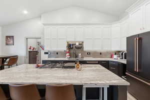Kitchen with high quality fridge, a breakfast bar, a center island, light stone counters, and vaulted ceiling