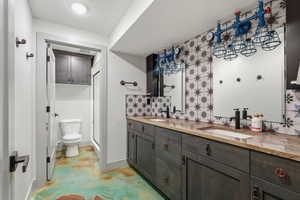 Bathroom with double vanity, backsplash, concrete flooring, and a shower stall