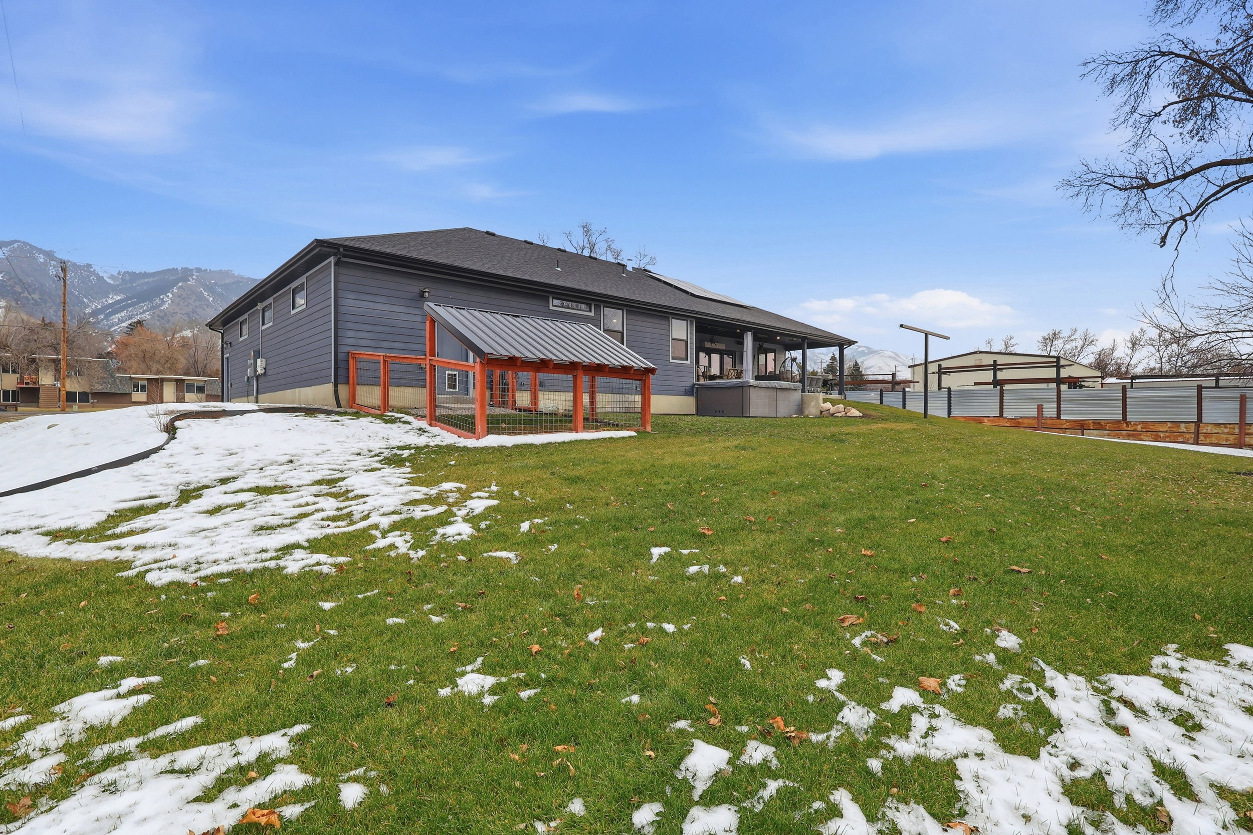 Snow covered property with a lawn and a dog run and covered back deck.