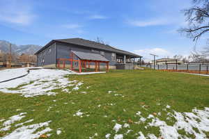 Snow covered property with a lawn and a dog run and covered back deck.