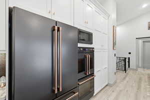 Kitchen with black appliances, white cabinetry, double oven, light wood-type flooring, recessed lighting, and lofted ceiling