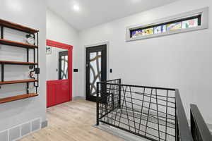 Entrance foyer with light wood-type flooring, custom metal railing, a hidden door and vaulted ceiling