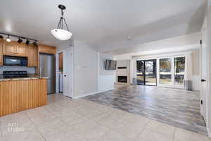Kitchen featuring light tile patterned floors, black appliances, light stone counters, a fireplace with raised hearth, and open floor plan