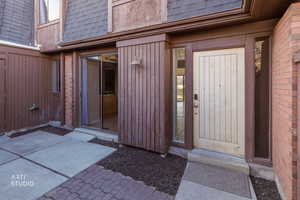 View of exterior entry with roof with shingles, mansard roof, and brick siding