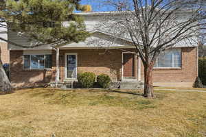 Millcreek Home with a front lawn, brick siding, and a covered porch