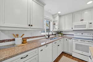 Kitchen featuring white appliances, light stone countertops, white cabinets, and dark wood-style floors