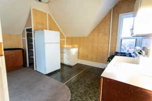 Kitchen featuring wallpapered walls, freestanding refrigerator, light countertops, white cabinets, and lofted ceiling