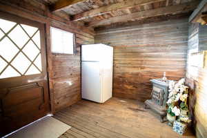 Entryway with a wooden ceiling with exposed beams, wood-type flooring, a wood stove, and wooden walls