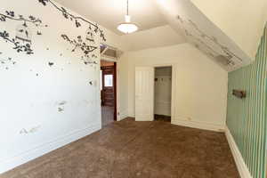 Unfurnished bedroom featuring dark carpet, a closet, vaulted ceiling, and wallpapered walls