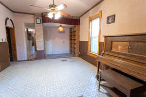 Interior space featuring a wainscoted wall, wooden walls, ceiling fan, and ornamental molding