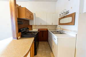 Kitchen featuring black / electric stove, light countertops, white cabinets, and light floors