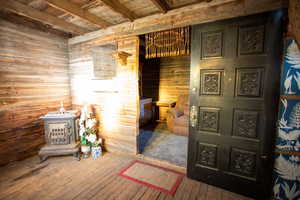 Bedroom featuring wooden walls, wood-type flooring, a wood stove, and a wood ceiling with exposed beams