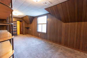 Additional living space with carpet flooring, wooden walls, and vaulted ceiling