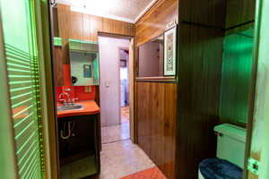 Half bathroom featuring wood walls, vanity, light tile patterned flooring, and crown molding