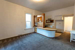 Kitchen featuring light countertops, open shelves, dark colored carpet, white cabinets, and a peninsula