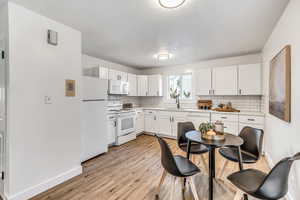 Kitchen with white appliances, light countertops, light wood-style floors, and white cabinets