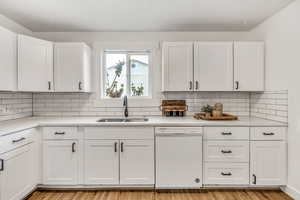 Kitchen with white dishwasher, white cabinets, decorative backsplash, and light stone counters