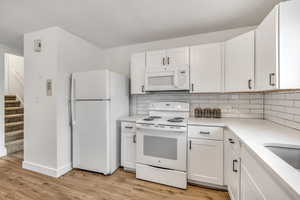 Kitchen featuring white appliances, white cabinets, backsplash, and light wood finished floors