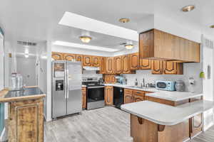 Kitchen with stainless steel appliances, light countertops, wood finish cabinetry, a kitchen breakfast bar, and a peninsula