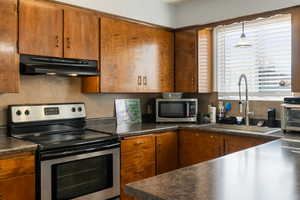 Kitchen with dark countertops, stainless steel appliances, wood finish cabinets, and hanging light fixtures