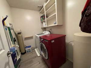 Laundry area with a textured ceiling, light wood-type flooring, and washer and dryer