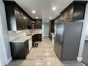 Kitchen with light stone counters, stainless steel fridge with ice dispenser, dark wood finish cabinetry, light wood-style floors, and glass fronted cabinets