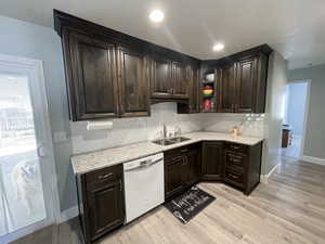 Kitchen featuring dark wood finish cabinetry, light stone counters, dishwashing machine, tasteful backsplash, and recessed lighting
