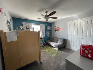 Living area with dark colored carpet, a textured ceiling, and a ceiling fan