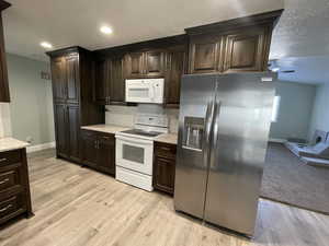Kitchen with white appliances, dark wood finish cabinetry, light wood-type flooring, decorative backsplash, and a textured ceiling
