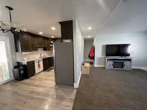 Kitchen featuring dark wood finish cabinetry, freestanding refrigerator, dishwasher, decorative backsplash, and recessed lighting