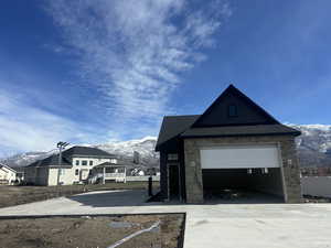 Detached garage at back of lot. View of side of home with a mountain view, stone siding, concrete driveway, and an outdoor structure