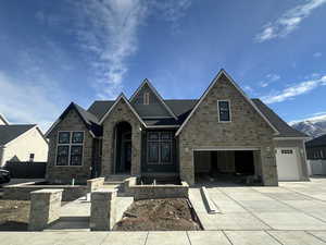 View of front facade featuring stone siding, concrete driveway, and roof with shingles