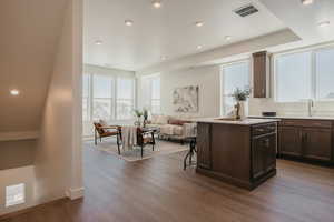 Kitchen with recessed lighting, a kitchen island, a kitchen bar, dark wood finish cabinets, and dark wood-style floors