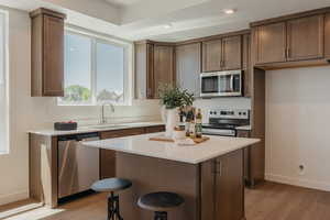 Kitchen with stainless steel appliances, light wood-style flooring, a center island, light stone countertops, and a kitchen bar