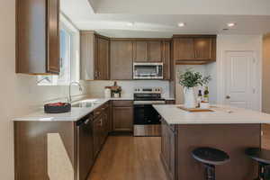 Kitchen with stainless steel appliances, wood finished floors, a kitchen breakfast bar, a center island, and recessed lighting