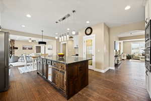 Kitchen featuring open floor plan, dark stone countertops, dark wood-style floors, and decorative light fixtures