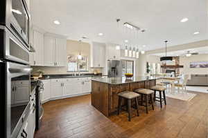 Kitchen with hanging light fixtures, open floor plan, dual tone cabinets, dark wood finished floors, and a stone fireplace