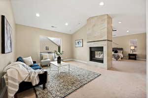 Living room with vaulted ceiling, light carpet, a fireplace, and recessed lighting