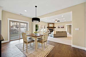 Dining space featuring dark wood-style flooring, a stone fireplace, ceiling fan, and recessed lighting